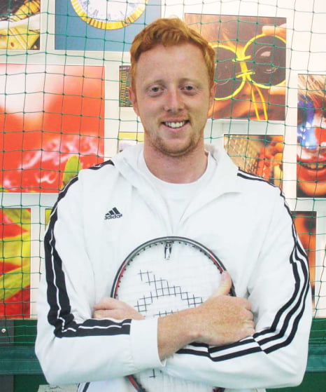 Jack Lane holding a tennis racquet stands in front of brightly coloured photos